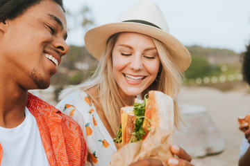 Couple dating and eating sandwiches at a beach picnic