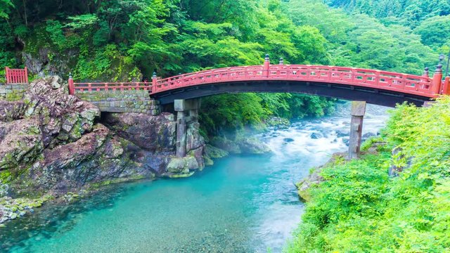 Day to night transition time-lapse of evening floodlights illuminating the ancient Shinkyo Sacred Bridge above flowing Daiya river and mist with nobody present in Nikko, Japan. Zoom out 4k at 30fps