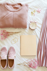 Flatlay of women knitted sweater, skirt, book, shoes, alarm clock, flowers on a pink fur background