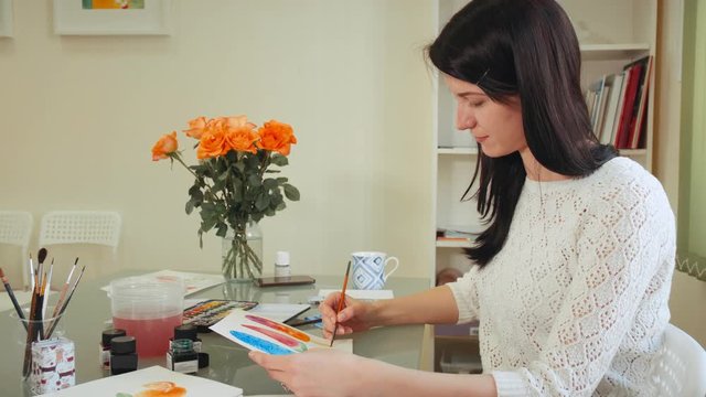 Young woman artist draw picture with watercolor paints and brush at the table.