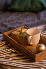 Winter decor: cup of coffee, a gift, a tray, a ball and a cozy striped plaid. Selected focus