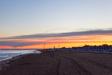 Italian summer beach covered with lonely deck chairs, calm sea, sunset in the background. 