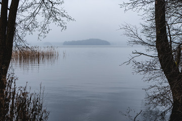 View of a lake surrounded by trees, winter dark and cold afternoon.
