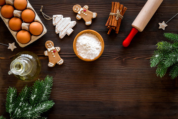 Fototapeta na wymiar Cook homemade gingerbread cookies for New Year party. Rolling pin, eggs, flour, cinnamon near gingerbread man and spruce branch on dark wooden background top view copy space