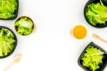 Healthy fast food concept. Light meal with lettuce in plastic containers near wooden spoons and green tea on white background top view space for text