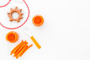 Healthy food for small babies. Carrot puree in bowl near bib, carrot slices, spoon on white background top view copy space