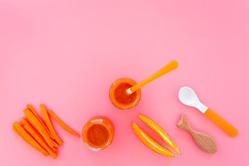 Healthy food for small babies. Carrot and pumpkin puree in bowl near carrot slices, spoon on pink background top view copy space