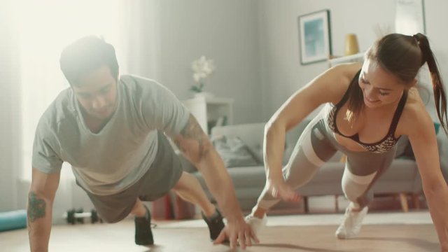 Strong and Beautiful Athletic Fitness Couple in Workout Clothes Doing Push Up Exercises and Giving Each Other a High Five in Their Bright and Spacious Living Room with Minimalistic Interior.