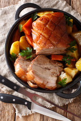 Krustenbraten Pork Roast with Crispy Rind with vegetables close-up in a frying pan. Vertical top view