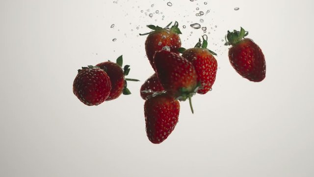 SLOW MOTION: Strawberries fall in water on white background