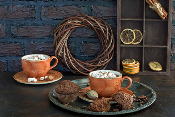 on the table are two cups of hot chocolate with marshmallows and muffins
