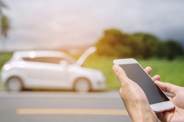 close up woman hand using a mobile smart phone call a car mechanic ask for help assistance because car broken roadside. people journey standing wait beside road broken car background.