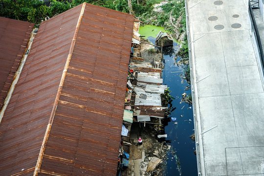 slum zone, photo shooting from top view, can see rust rooftop, garbage and dirty water beside building.