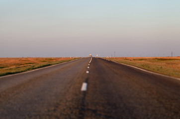 Fototapeta na wymiar An empty asphalt road in the steppe at sunset. The Astrakhan region. Russia. Tilt-shift effect.