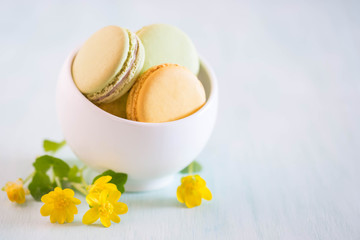 Obraz na płótnie Canvas Macarons on white wooden table and beauty yellow flowers