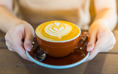 Close up of female hand serving coffee with latte art in the morning. Focus on female hands placing a cup of coffee.