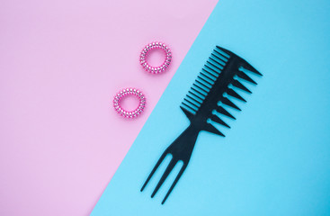 Black plastic comb and two pink scrunchies on blue and pink background.