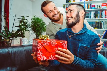 Surprised young handsome gay couple in love smiling looking at each other celebrating and giving gift