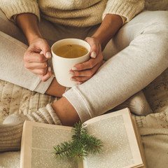 Cozy home. Beautiful girl is reading a book on the bed. Good morning with tea. Pretty young girl relaxing. The concept of reading