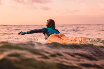 Surfer woman with perfect body on a surfboard floating in ocean. Surfing at sunset
