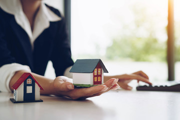 Woman holds a house model in her hand and using calculator . Buy real estate. Real estate services for buying your home. Loan for the purchase of housing.home loan and insurance concept.