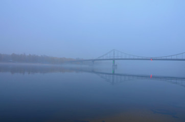 Fototapeta na wymiar Mysterious foggy landscape view of Pedestrian Bridge over Dnieper River in Kyiv. Autumn morning view. Kyiv, Ukraine