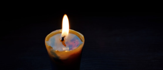 One handmade candle flame burning in darkness closeup panoramic view with copy space for text.