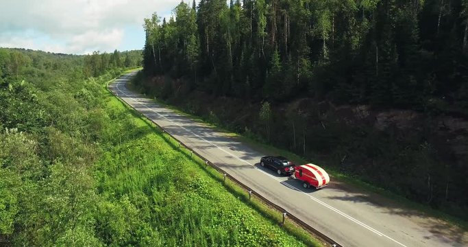 One Black Car with Funny Tear Trailer driving on Winding Freeway in Forest Mountains - Aerial Drone View