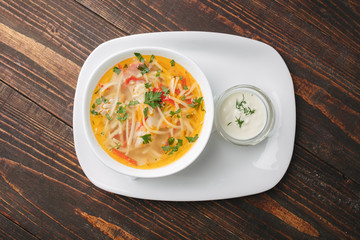 Chicken soup on a white plate served with sour cream