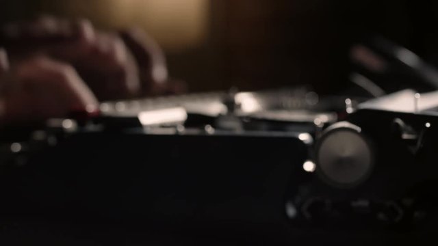 Hands typing on a vintage typewriter with the carriage return knob pulling out of focus