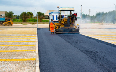 Asphalt paver with asphalt heated to temperatures above 160 ° during road at the construction. Road specialized equipment is laying the way.