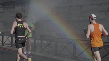 Slow motion shot of marathon runners passing by a sprinkler that creates a rainbow