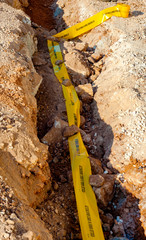 excavation with a narrow section to bury corrugated plastic cable ducts for fiber optic network..Yellow ribbon with the inscription 