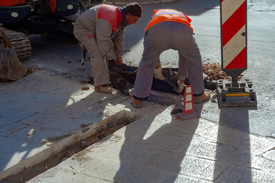 Execution of fiber optic distribution network for telecommunications. Workers position the cast iron manhole covers on manholes