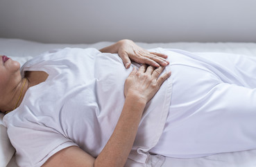 Elderly woman having painful stomachache on bedroom