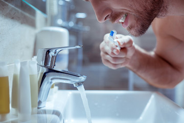 Young handsome bearded man brushing his teeth before going to bed