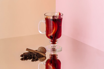 Mulled wine in glass with cinnamon stick, christmas sweets on on the glass table and fruits and ginger on background. Winter concept