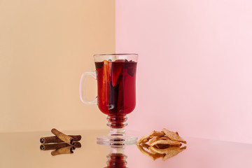 Mulled wine in glass with cinnamon stick, christmas sweets on on the glass table and fruits and ginger on background. Winter concept