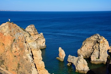 Elevated view of a tourist standing on the cliffs with views over the ocean, Ponda da Piedade, Lagos, Portugal.
