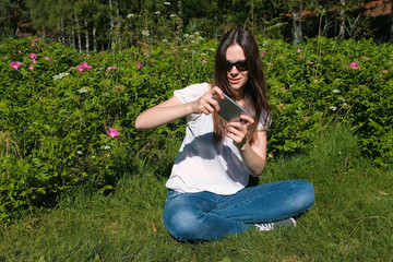 Fototapeta premium Woman is playing a game on mobile phone sitting in park in sunny day.