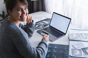 woman sitting at home. laptop with white screen. medicine documents on the table.