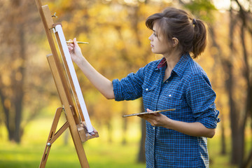 woman artist drawing a picture on an easel in nature, a girl with a brush and a palette, a concept of creativity and a hobby