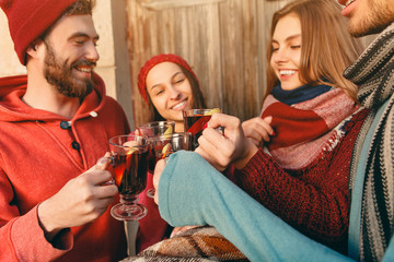 Smiling european men and women during party photoshoot. The guys posing as friends at studio fest with wineglasses with hot mulled wine on foreground.
