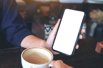 Mockup image of a woman holding and showing black mobile phone with blank screen to someone on the table in cafe
