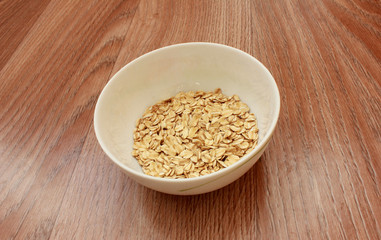Oat flakes in a white bowl on wood
