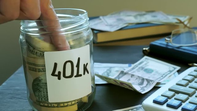 Hand is putting money in jar with sign 401k. Retirement plan.