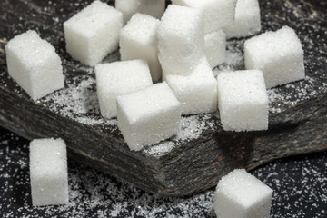 Sugar cubes and granulated sugar on black rock slate.
