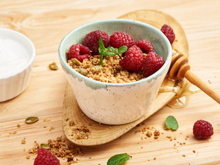 Homemade granola and yogurt in a bowl with raspberries on a wooden table.