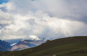 Green hill with snow peaks and coluds background