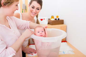 Smiling mother looking at woman holding baby in the bucket for bathing